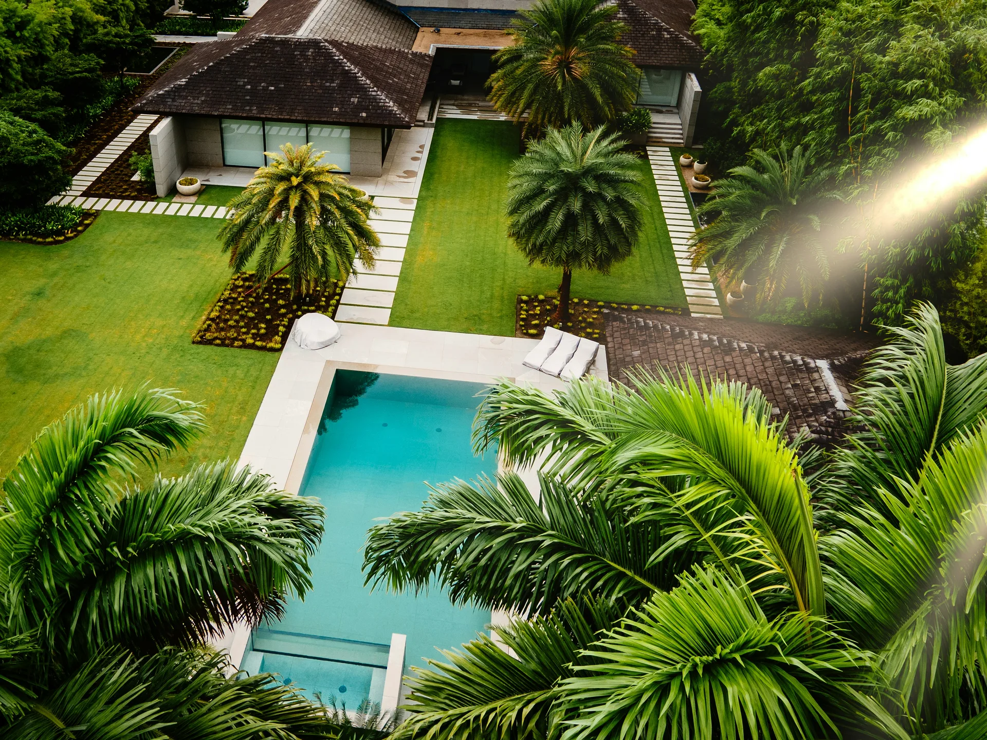 A villa and turquoise swimming pool surrounded by palms and lush green gardens