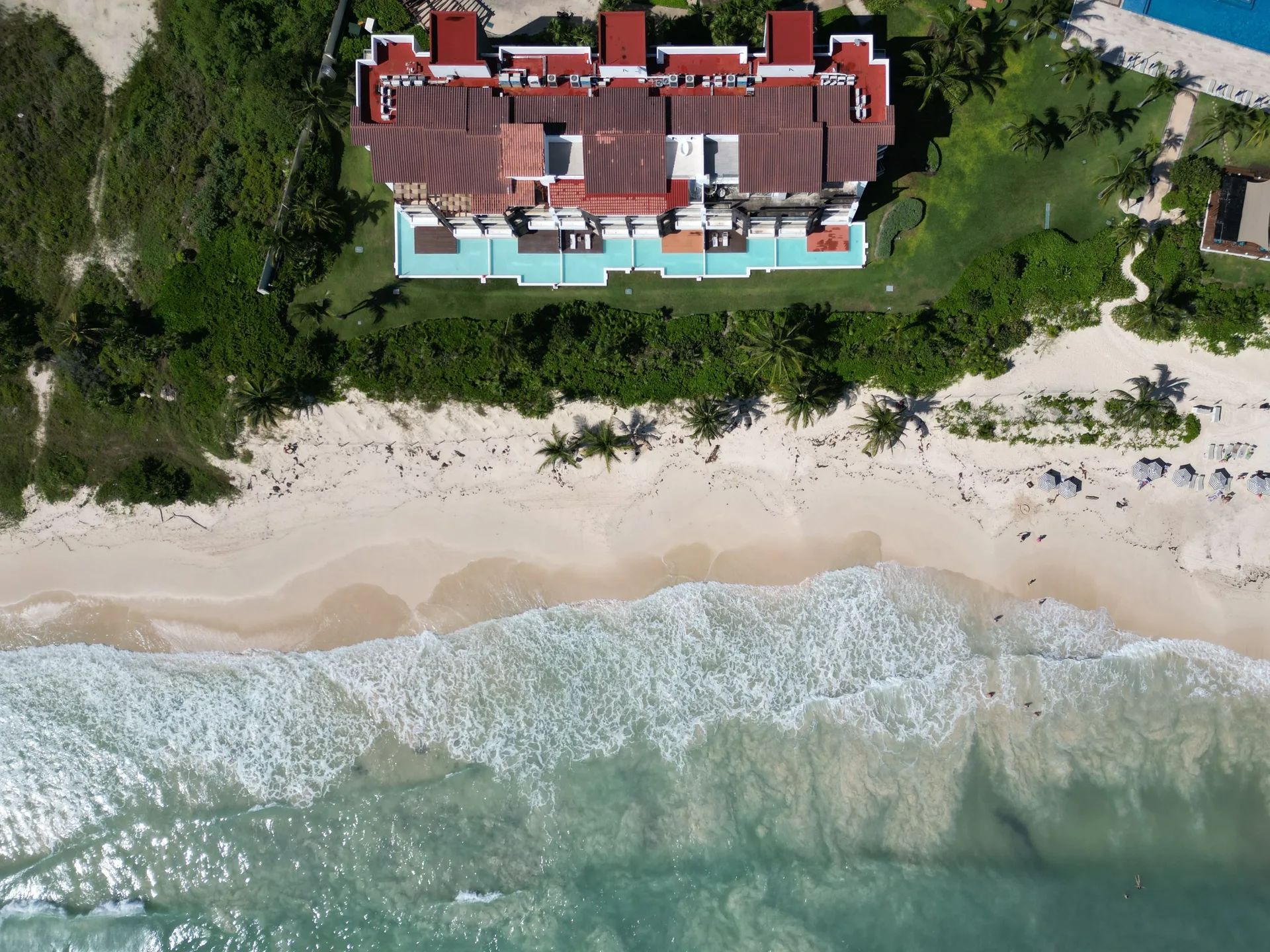 A beachfront mansion with a pool and palms above the white sand and waves of Playa del Carmen